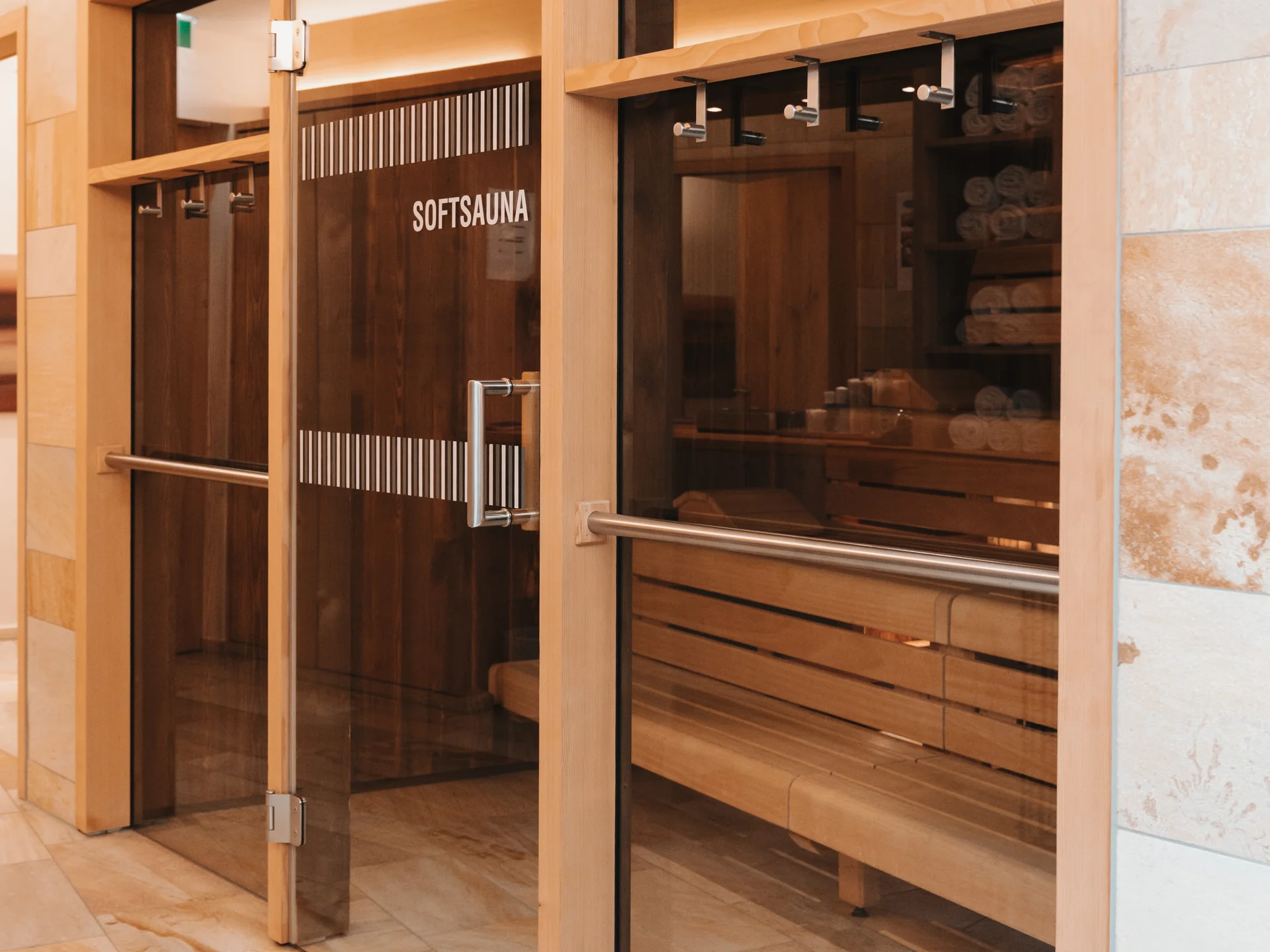Gläserner Eingang zur Softsauna mit Holzbänken und hellen Steinfliesen