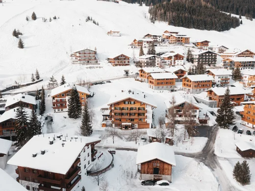 Hotel am Arlberg mit Aussicht | Hotel Panorama Lech Verschneites Bergdorf mit Holzhäusern und bewaldeten Hängen aus der Vogelperspektive