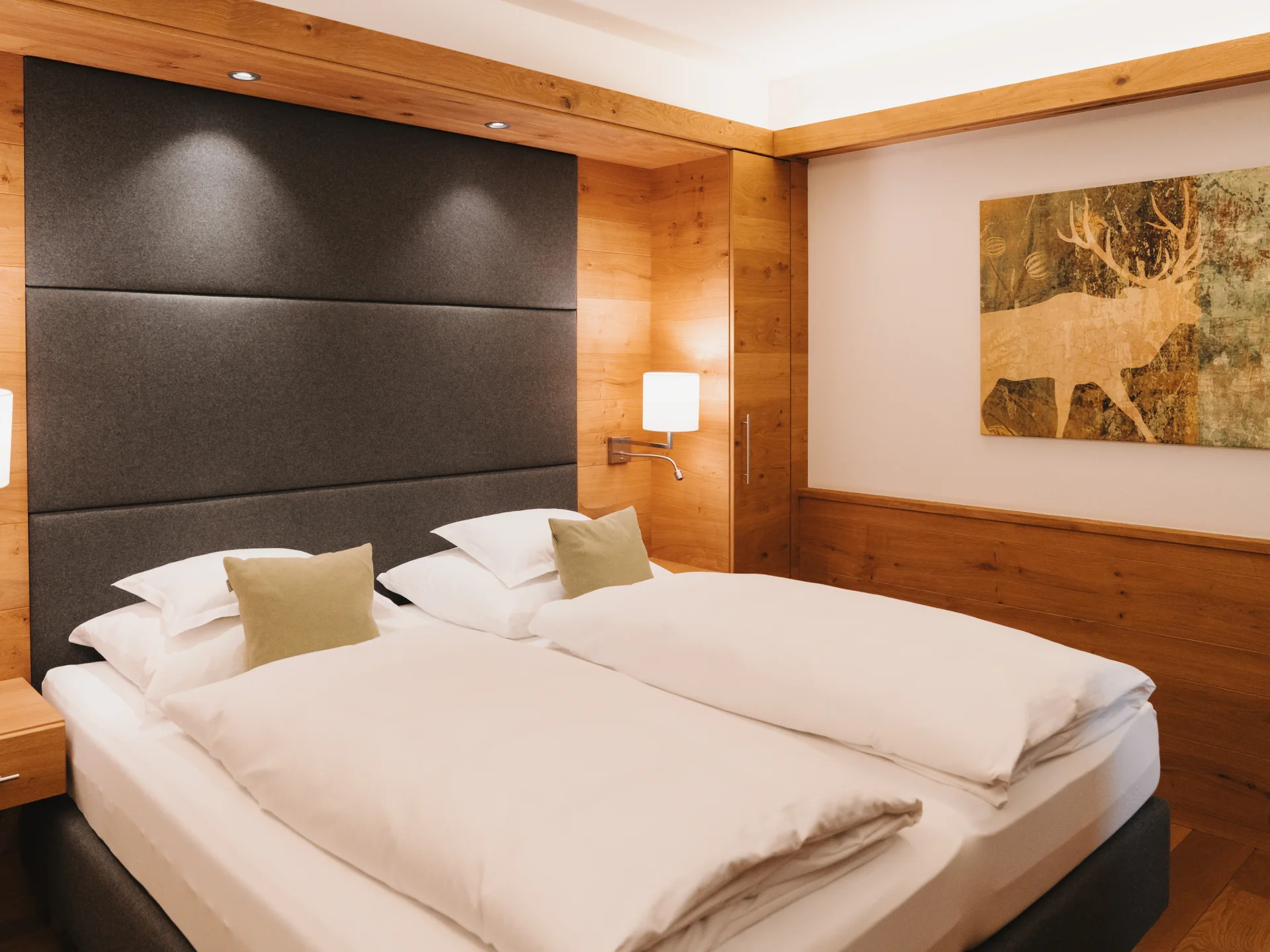 Hotelzimmer mit zwei weißen Betten, dunklem Kopfteil und warmen Holzvertäfelungen