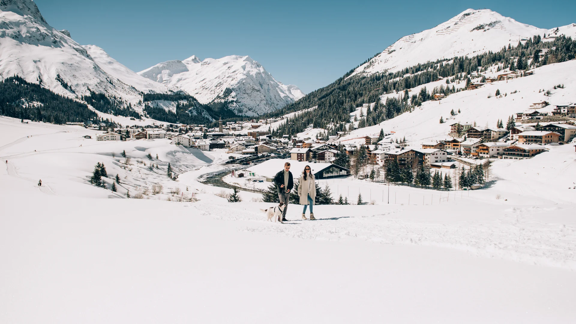 Picture gallery | Hotel Panorama in Lech am Arlberg Couple walking a dog in the snow above a village in the snowy Alps