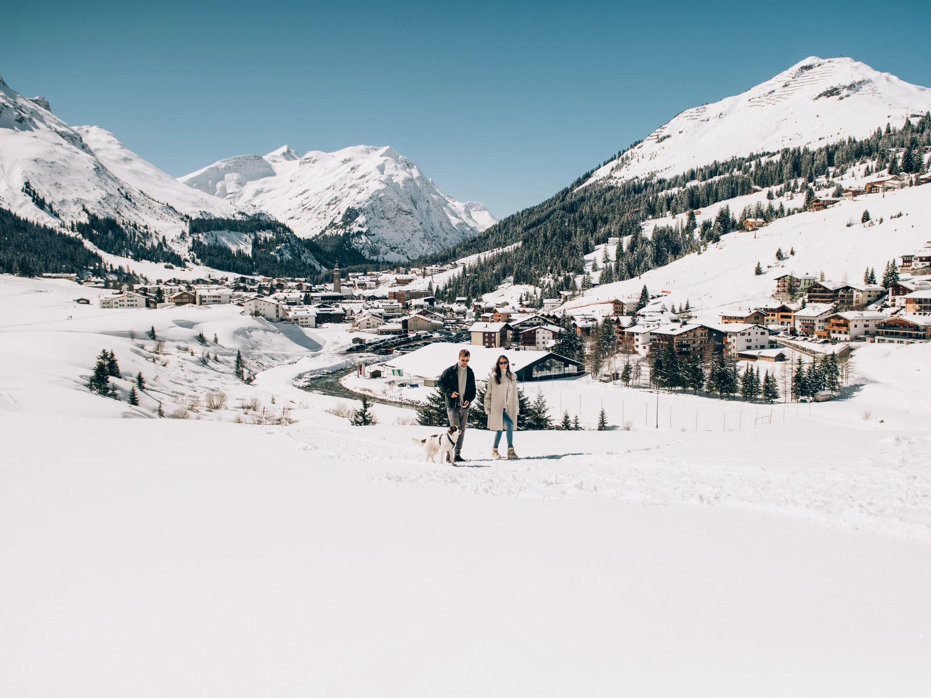 A ski holiday in Lech at Hotel Panorama Couple walking a dog in the snow above a village in the snowy Alps