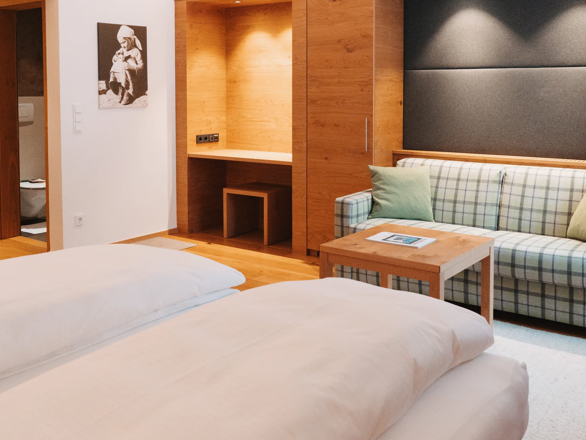 Hotelzimmer mit großem Bett, kariertem Sofa und hölzerner Einbaunische