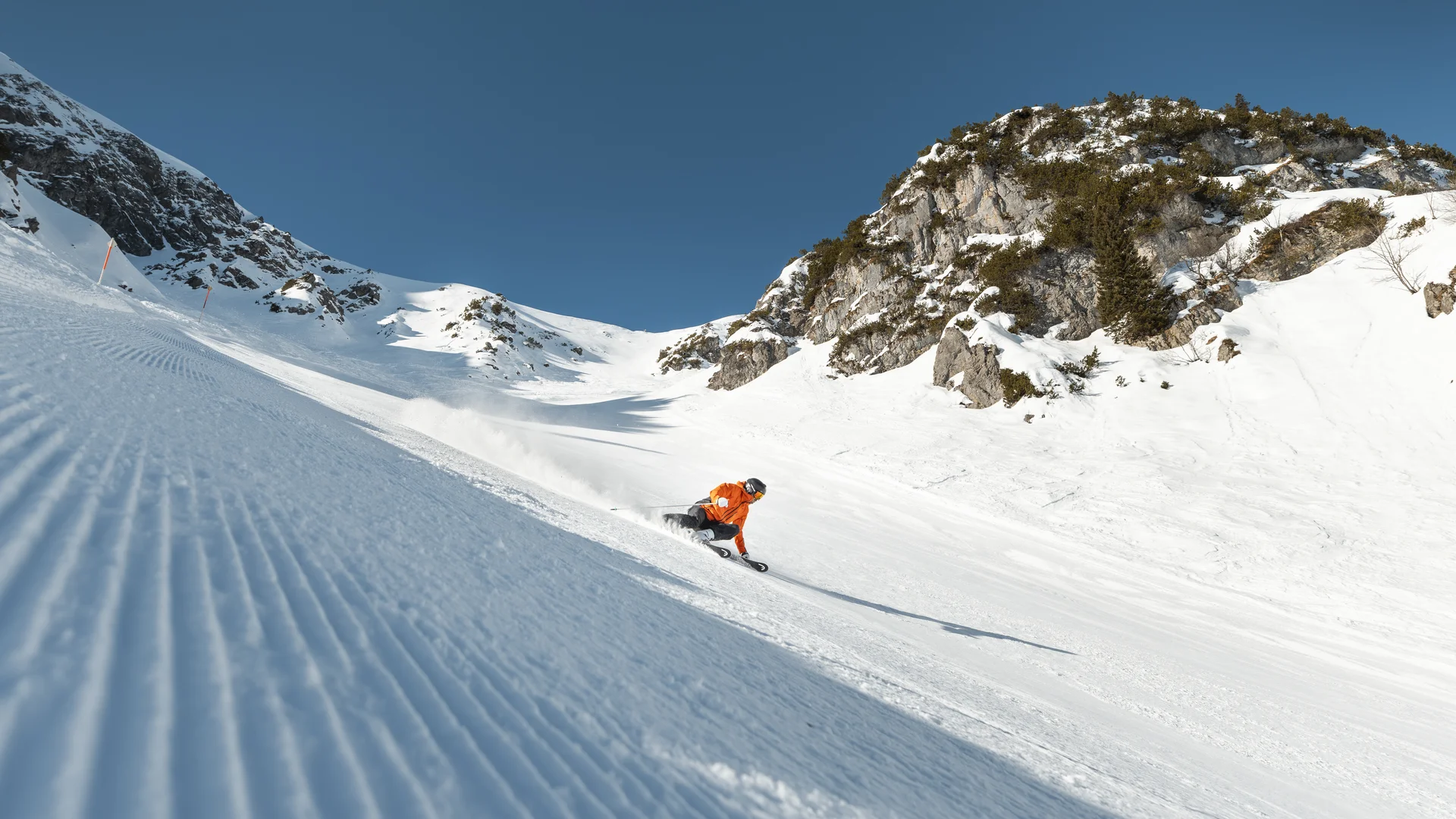 Picture gallery | Hotel Panorama in Lech am Arlberg Skier in an orange jacket descends a groomed slope between snow-covered mountain peaks