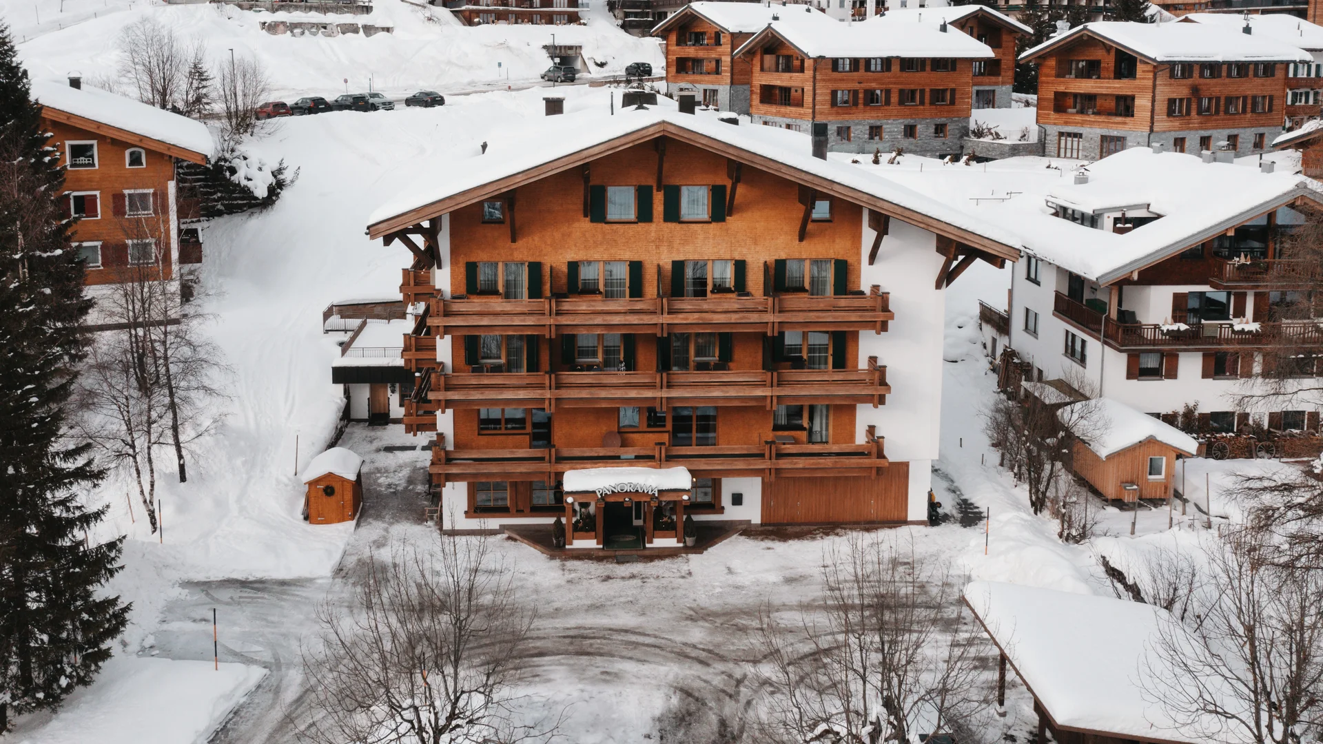 Picture gallery | Hotel Panorama in Lech am Arlberg Wooden chalet with balconies in a snowy mountain village, surrounded by other buildings