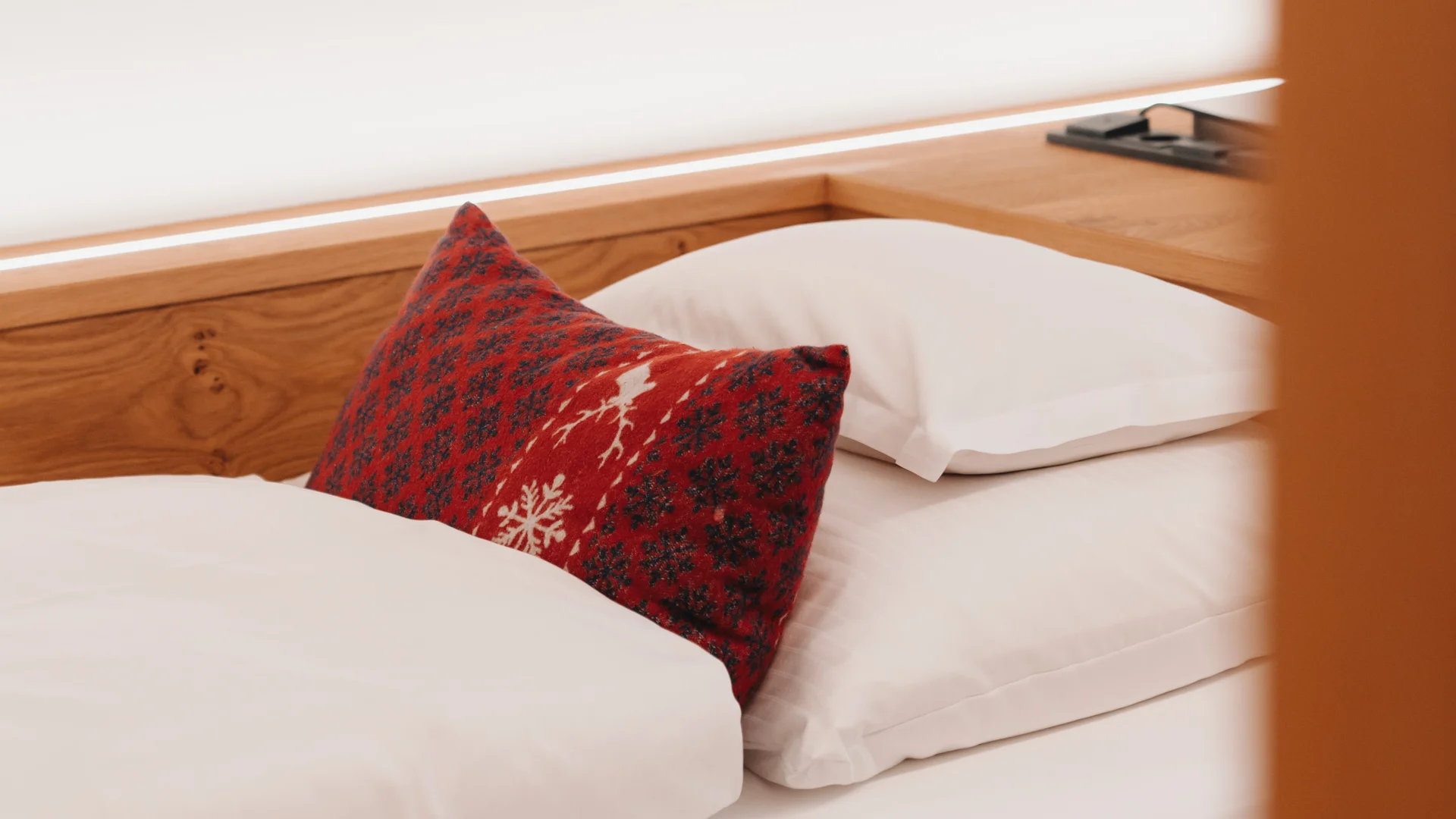 Hotel am Arlberg mit Aussicht | Hotel Panorama Lech Holzbett mit weißer Bettwäsche und roten, gemusterten Zierkissen