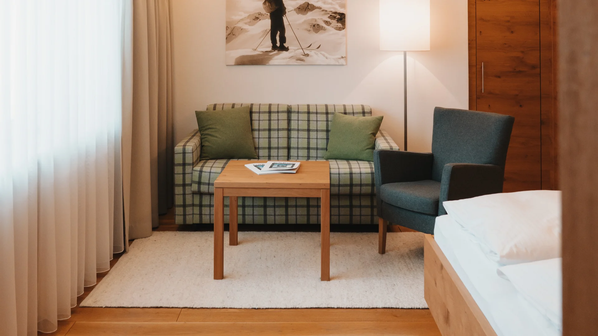 Hotel room with a bed, plaid sofa, armchair and wooden floor