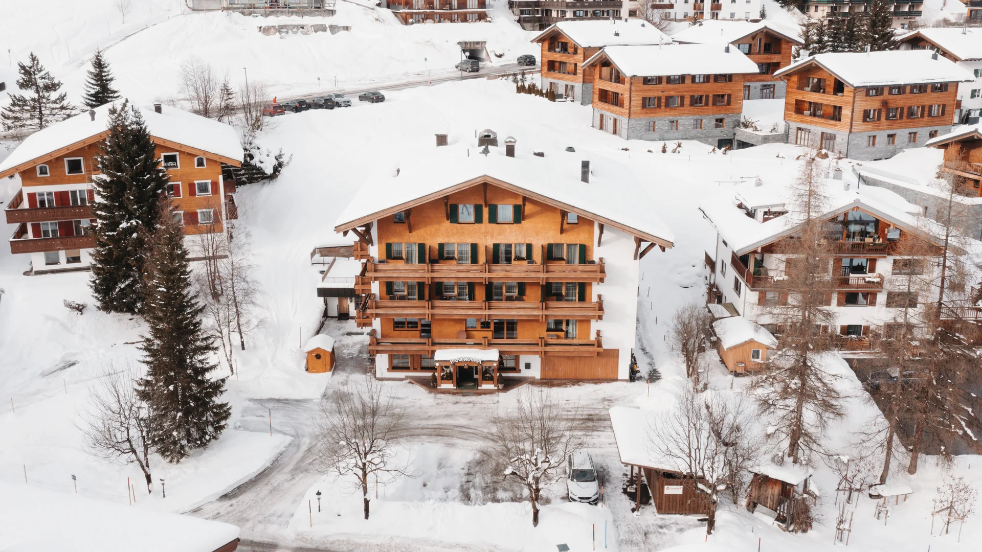 Snow-covered alpine village with wooden chalets and fir trees, viewed from above