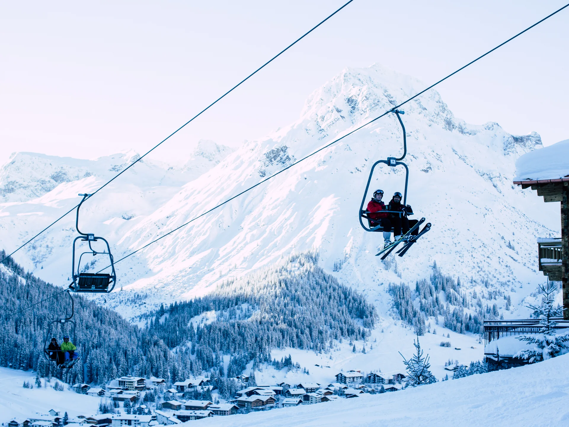 The journey to your hotel in Vorarlberg | Hotel Panorama Ski lift carrying skiers past a snowy mountain and a village in the valley