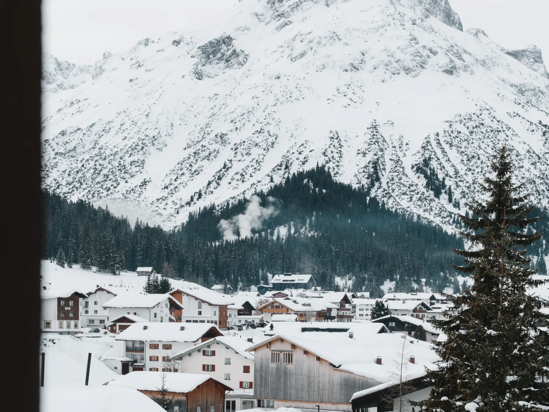 The journey to your hotel in Vorarlberg | Hotel Panorama Snow-covered mountain village beneath a towering peak, framed by a window