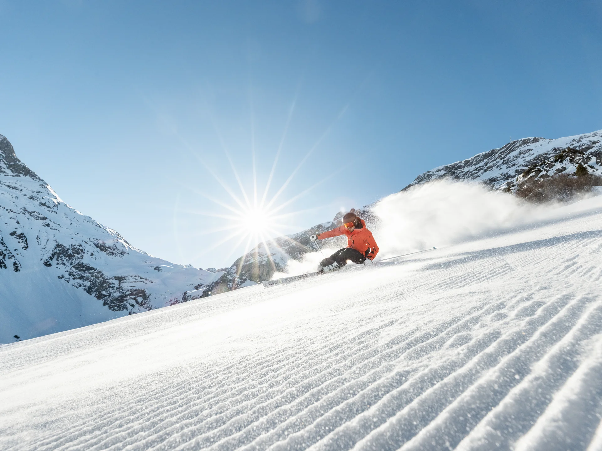 The journey to your hotel in Vorarlberg | Hotel Panorama Skier in an orange jacket carving down a snowy slope in bright sunshine