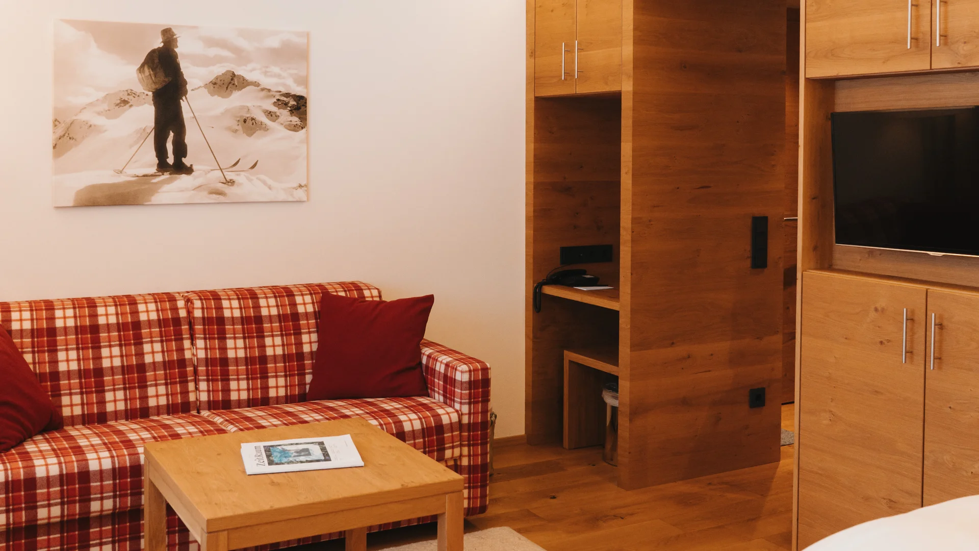 Picture gallery | Hotel Panorama in Lech am Arlberg Hotel room with a white bed, plaid sofa, wooden table and built-in cabinet with TV