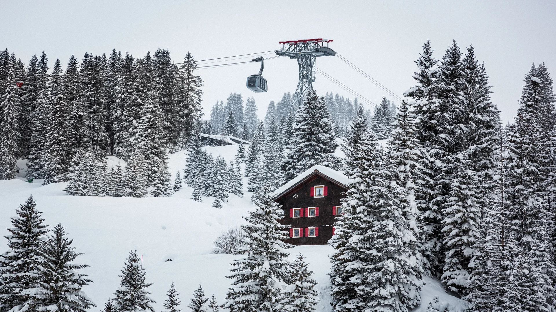 Picture gallery | Hotel Panorama in Lech am Arlberg Snow-covered mountain cabin among fir trees, with a gondola overhead
