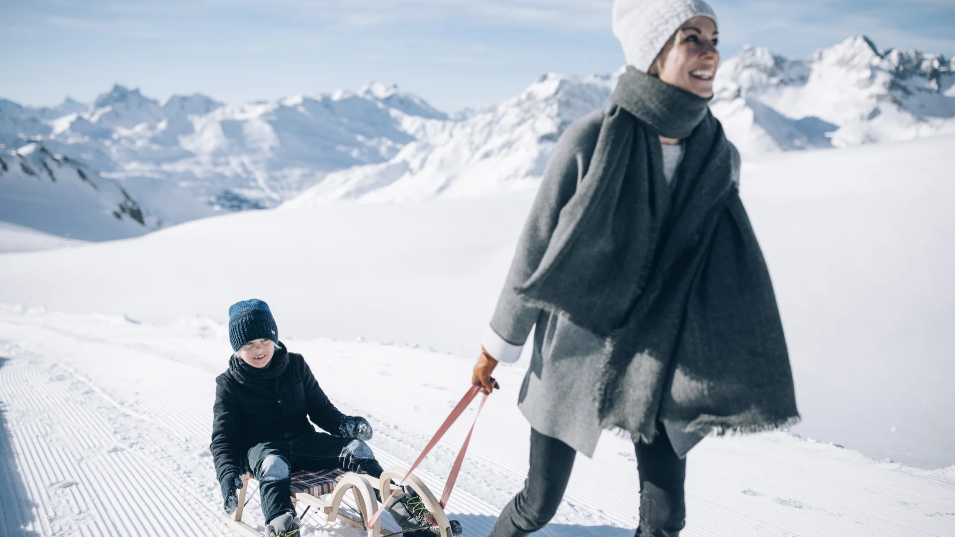 Picture gallery | Hotel Panorama in Lech am Arlberg Woman pulls a child on a sled through a snowy mountain landscape