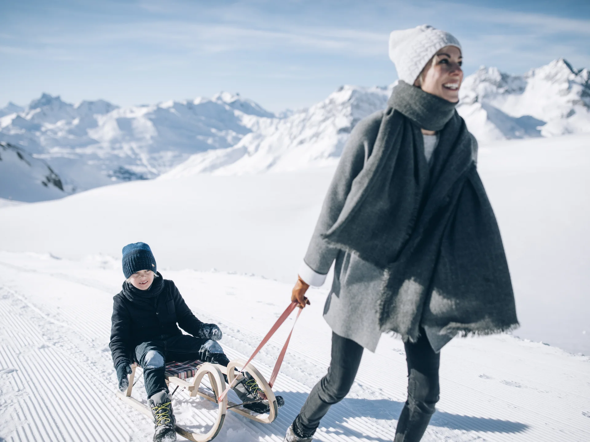 A ski holiday in Lech at Hotel Panorama Woman pulls a child on a sled through a snowy mountain landscape