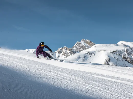 A ski holiday in Lech at Hotel Panorama Skier carves down a groomed slope with snow-covered mountains in the background