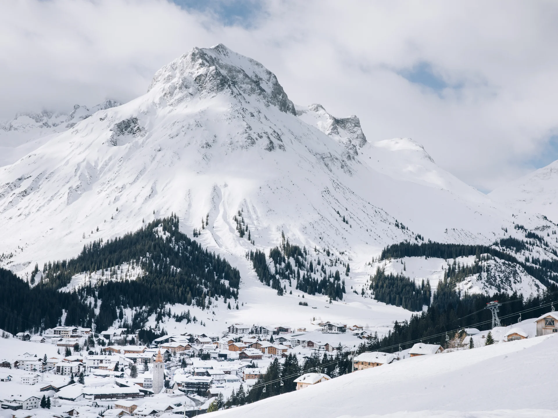 A ski holiday in Lech at Hotel Panorama Snow-covered mountain village beneath a high peak, with ski slopes and forested hillsides