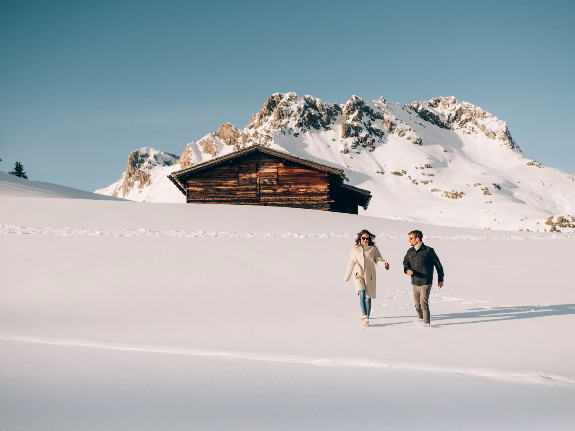 A ski holiday in Lech at Hotel Panorama Two people walk through a snowy landscape with a mountain hut and snow-covered peaks