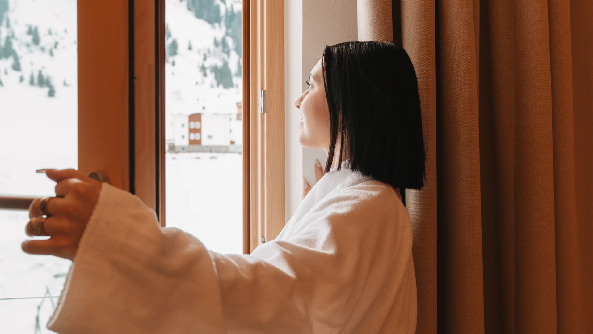 Picture gallery | Hotel Panorama in Lech am Arlberg Woman in a white bathrobe looks out the window at a snowy mountain landscape