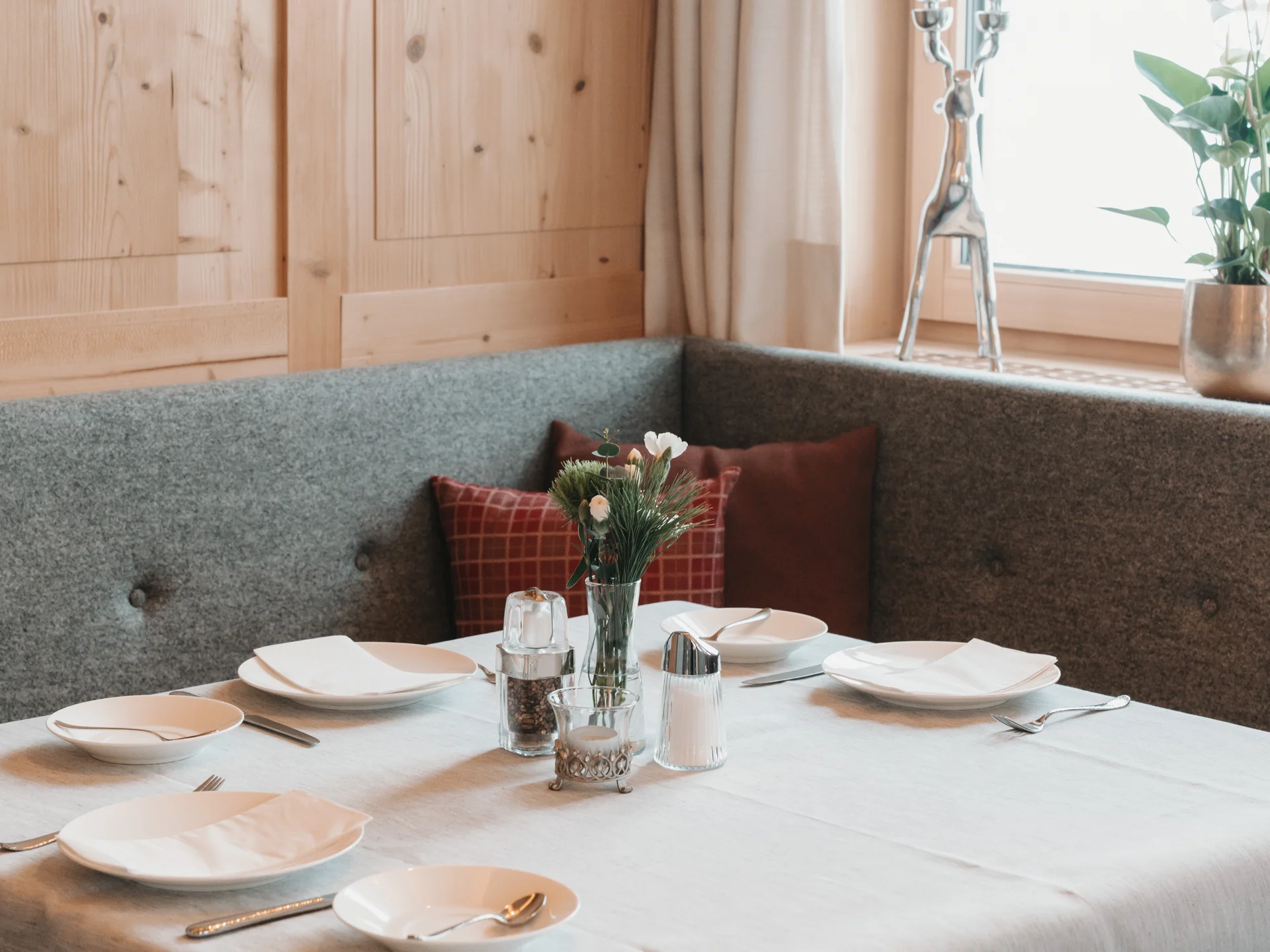 Gedeckter Tisch in einer gemütlichen Sitzecke mit Holzverkleidung und Blumen