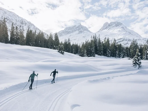 A ski holiday in Lech at Hotel Panorama Two cross-country skiers on a snowy trail beneath winter mountains and among fir trees