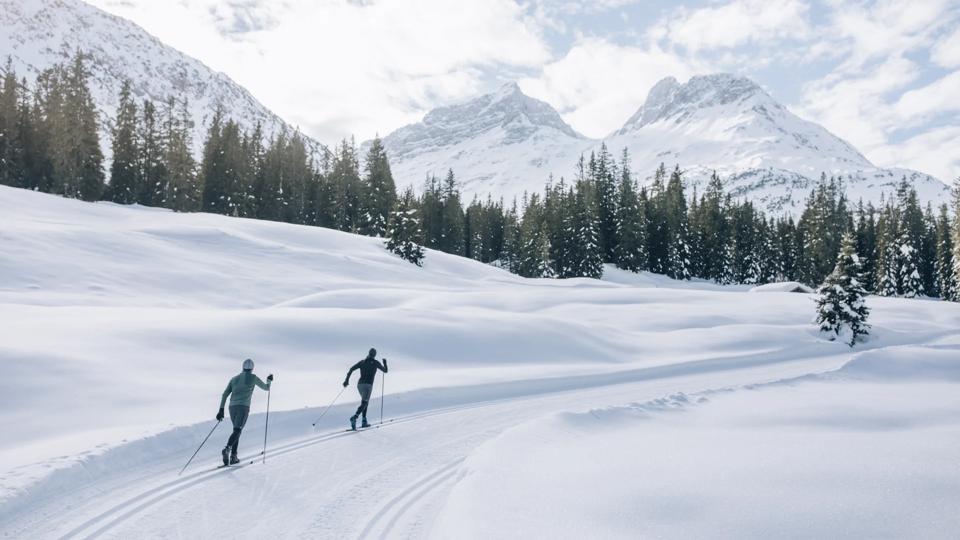 Picture gallery | Hotel Panorama in Lech am Arlberg Two cross-country skiers on a snowy trail beneath winter mountains and among fir trees