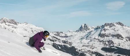 Skier crouches low while descending a snowy slope against an alpine mountain backdrop