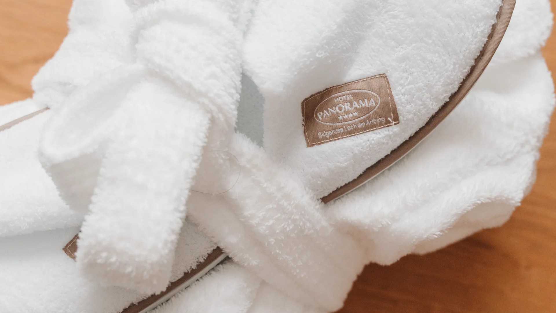 Picture gallery | Hotel Panorama in Lech am Arlberg White terry hotel slippers with brown trim on a wooden floor
